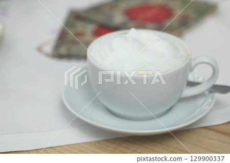 White coffee cup with foam on top sits on a white saucer White coffee cup with foam on top sits on a white saucer 129900337
