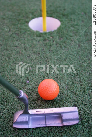 Golf ball is sitting on a green field next to a golf club 129900378