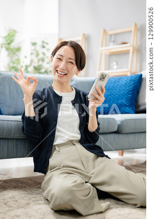 拿著智能手機和給一個好標誌的婦女 129900526