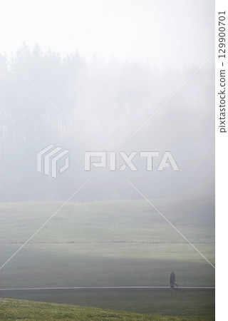 Person is walking in a field with foggy weather 129900701
