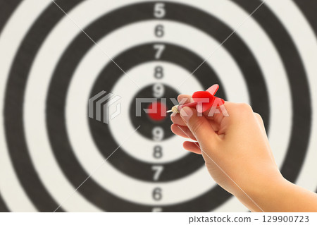 A hand releases a red dart aimed at a bullseye target on a wall A hand releases a red dart aimed at a bullseye target on a wall 129900723