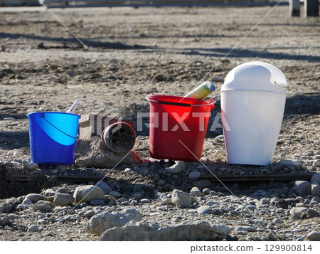 Three buckets of different colors are sitting on a rocky ground 129900814