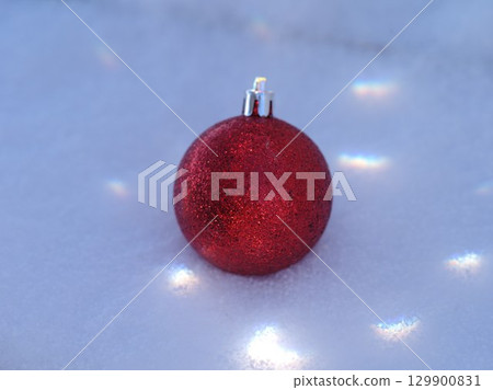 Red ornament is sitting on top of a snowy surface Red ornament is sitting on top of a snowy surface 129900831