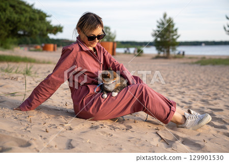 Cat watching woman owner relaxing on sandy beach on seaside walk. Shore stroll with pet feline 129901530