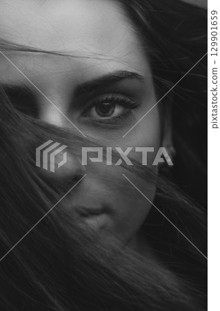 Woman portrait with part face covered with hairs by blowing wind Woman portrait with part face covered with hairs by blowing wind 129901659