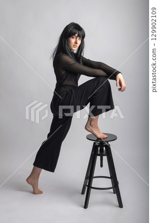 Woman portrait with dark hairs and clothes with one leg on chair 129902109