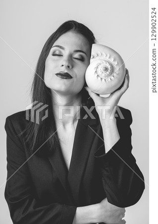 Woman listen sea rustle in seashell near her ear with closed eyes 129902524