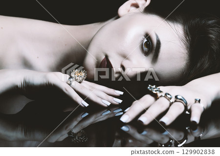 Studio portrait of beautiful and sexy brunette woman with fancy make-up and various rings on her fingers 129902838