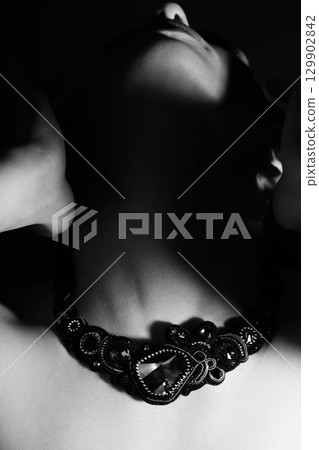 Part of woman face silhouette with black necklace hiding in shade 129902842