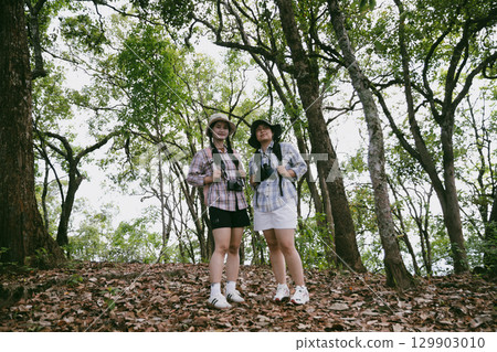Two female friends with backpacks on vacation hiking through countryside together. Asian friend girls backpacker friend travel in forest wild together. happy and enjoying sunny day while hiking. Two female friends with backpacks on vacation hiking through countryside together. Asian friend girls backpacker friend travel in forest wild together. happy and enjoying sunny day while hiking. 129903010