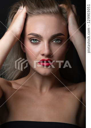 Studio portrait of beautiful blonde woman brushing her hair with fingers Studio portrait of beautiful blonde woman brushing her hair with fingers 129903051