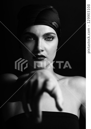 Studio portrait of beautiful woman with scarf on her head pointing finger to camera Studio portrait of beautiful woman with scarf on her head pointing finger to camera 129903108