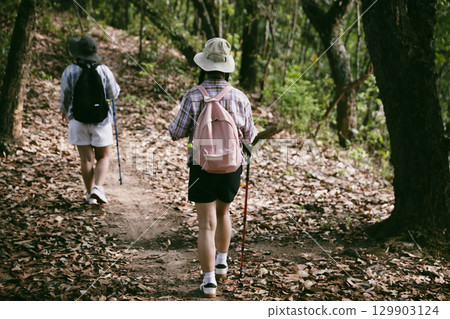 Two female friends with backpacks on vacation hiking through countryside together. Asian friend girls backpacker friend travel in forest wild together. happy and enjoying sunny day while hiking. Two female friends with backpacks on vacation hiking through countryside together. Asian friend girls backpacker friend travel in forest wild together. happy and enjoying sunny day while hiking. 129903124