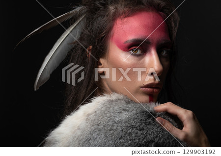 Studio portrait of woman with red Indian tribe make-up, dreadlocks and feathers in hair Studio portrait of woman with red Indian tribe make-up, dreadlocks and feathers in hair 129903192