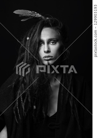 Studio portrait of woman with make-up, dreadlocks and feathers in hair 129903193