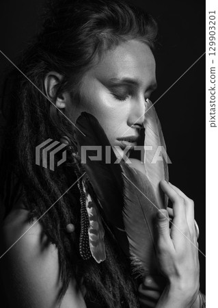 Studio portrait of woman with make-up, dreadlocks and bird feathers 129903201