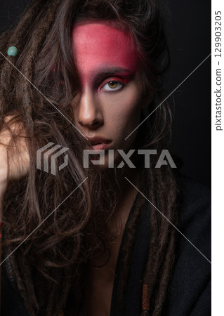 Studio portrait of woman with red Indian tribe make-up and hair with dreadlocks Studio portrait of woman with red Indian tribe make-up and hair with dreadlocks 129903205