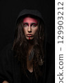 Model with tribe red make-up, dreadlocks, feather attached to her hair hiding under hood 129903212
