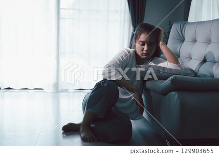 Tired depressed desperate tired girl sadly sitting on couch at home. Young woman is sitting on floor living room, feeling sad and depressed. Psychological problem. Depression and loneliness concept. 129903655