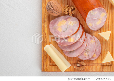 Sliced sausage with cheese cubes and walnuts on wooden board served with cheese pieces. top view. copy space Sliced sausage with cheese cubes and walnuts on wooden board served with cheese pieces. top view. copy space 129903679