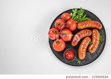 Grilled sausages with fresh tomatoes, parsley, and ketchup on black plate. top view. copy space Grilled sausages with fresh tomatoes, parsley, and ketchup on black plate. top view. copy space 129903684