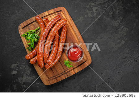 Grilled long sausages with ketchup and parsley on wooden board. top view. copy space Grilled long sausages with ketchup and parsley on wooden board. top view. copy space 129903692