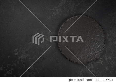 Empty round black stone plate on dark textured background. top view. copy space Empty round black stone plate on dark textured background. top view. copy space 129903695