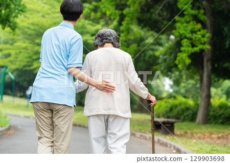 Rear view of a senior woman using a cane and her caregiver Rear view of a senior woman using a cane and her caregiver 129903698