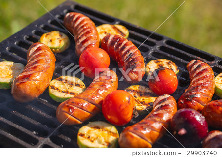Grilled sausages with vegetables and tomatoes sizzling on barbecue grill outdoors Grilled sausages with vegetables and tomatoes sizzling on barbecue grill outdoors 129903740