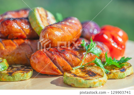 Grilled sausages with zucchini, bell pepper, and parsley on wooden board outdoors Grilled sausages with zucchini, bell pepper, and parsley on wooden board outdoors 129903741