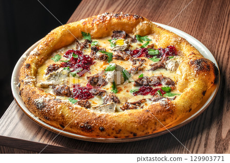 Gourmet pizza topped with slow-cooked beef, caramelized onions, herbs, and melted cheese on a golden crust 129903771