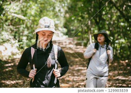 Two female friends with backpacks on vacation hiking through countryside together. Asian friend girls backpacker friend travel in forest wild together. happy and enjoying sunny day while hiking. Two female friends with backpacks on vacation hiking through countryside together. Asian friend girls backpacker friend travel in forest wild together. happy and enjoying sunny day while hiking. 129903839