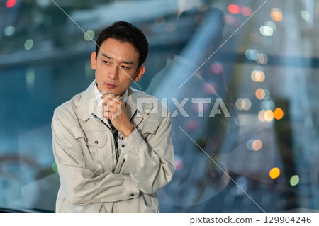 一位身著工作服的男子雙臂交叉，背對著摩天大樓思考著 129904246