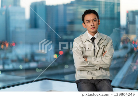 一位身著工作服的男子雙臂交叉,背對著摩天大樓思考著 一位身著工作服的男子雙臂交叉,背對著摩天大樓思考著 129904249