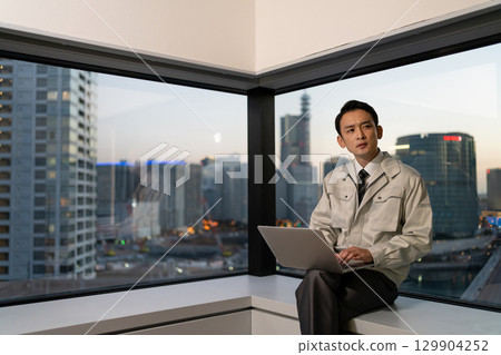 A man in work clothes operating a computer in an office 129904252