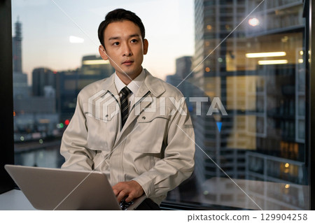 一名身穿工作服的男子在建築工地操作電腦 129904258