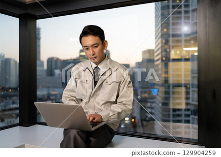 一名身穿工作服的男子在建築工地操作電腦 129904259