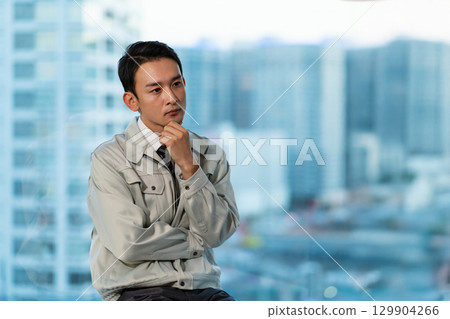 一名身穿工作服的男子雙手交叉，背景是摩天大樓 129904266