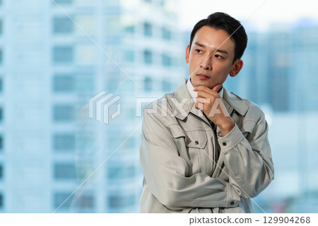 一位身穿工作服的男子一邊看著摩天大樓一邊思考 129904268