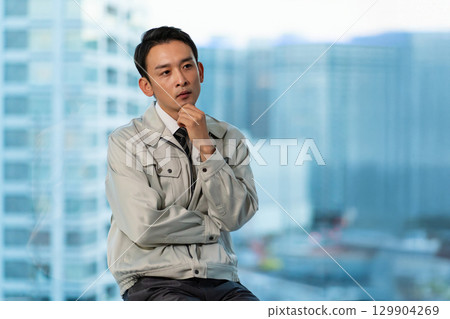 A man in work clothes thinking with his arms folded 129904269