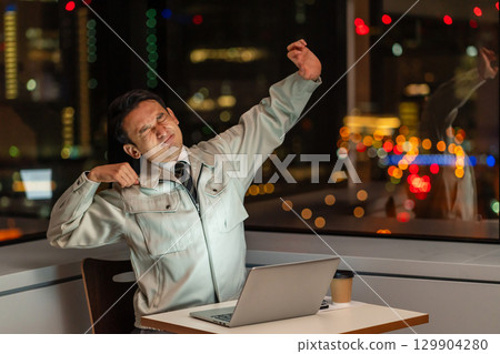 晚上，一位身穿工作服的男士在電腦前伸展身體 129904280