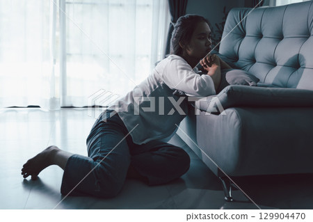 Tired depressed desperate tired girl sadly sitting on couch at home. Young woman is sitting on floor living room, feeling sad and depressed. Psychological problem. Depression and loneliness concept. Tired depressed desperate tired girl sadly sitting on couch at home. Young woman is sitting on floor living room, feeling sad and depressed. Psychological problem. Depression and loneliness concept. 129904470