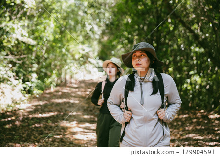 Two female friends with backpacks on vacation hiking through countryside together. Asian friend girls backpacker friend travel in forest wild together. happy and enjoying sunny day while hiking. 129904591