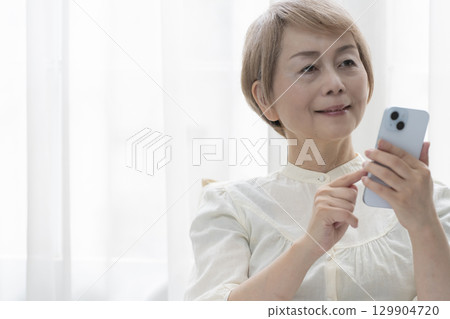 一位老年婦女在臥室的床上操作智慧型手機 129904720