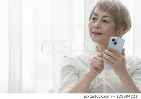 一位老年婦女在臥室的床上操作智慧型手機 129904721