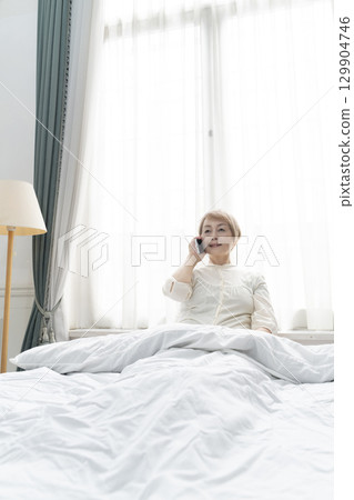 一位老年婦女在臥室的床上操作智慧型手機 129904746