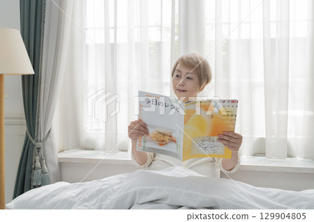 老年婦女在臥室的床上看雜誌 老年婦女在臥室的床上看雜誌 129904805