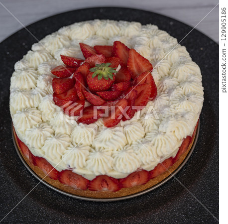 Delightful fraisier cake topped with fresh strawberries and whipped cream is served at a gathering 129905186