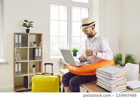 Funny man sitting at the desk of his workplace at office and booking tickets for summer vacation. Funny man sitting at the desk of his workplace at office and booking tickets for summer vacation. 129905486
