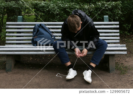 A teenage boy on a bench tying his shoelaces. 129905672